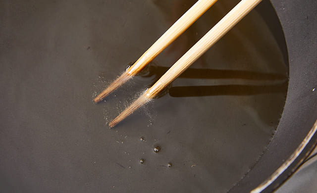 菜箸を揚げ油に入れている写真